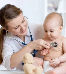 Pediatrician doctor gently examining a newborn baby with stethoscope during routine check-up, holding teddy bear on exam table at Ridansh Hospital, Lucknow.